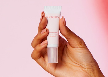 Against a pink backdrop, a hand holds a tube of Instant Puffiness Reducer.